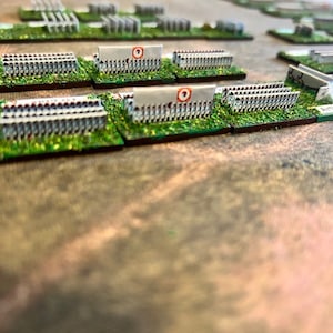 Op de afbeelding: Een close-up van verschillende geverfde miniatuur militaire figuren die in rijen op groene bases zijn gerangschikt. De figuren dragen witte uniformen en houden wapens vast. De figuren zijn gerangschikt in een formatie die lijkt op een Romeins legioen.
