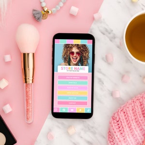 K&ouml;nnte beinhalten: Ein Smartphone, auf dem eine Website f&uuml;r ein Gesch&auml;ft namens "STORE NAME" angezeigt wird. Die Website enth&auml;lt Links zu "Besuchen Sie meine Website", "Shop Sale", "Shop Our Brand", "Was wir tun", "&Uuml;ber mich" und "Kontakt". Das Telefon befindet sich auf einer rosa und wei&szlig;en Oberfl&auml;che mit Make-up-Pinseln, einer Make-up-Palette und anderem Zubeh&ouml;r.