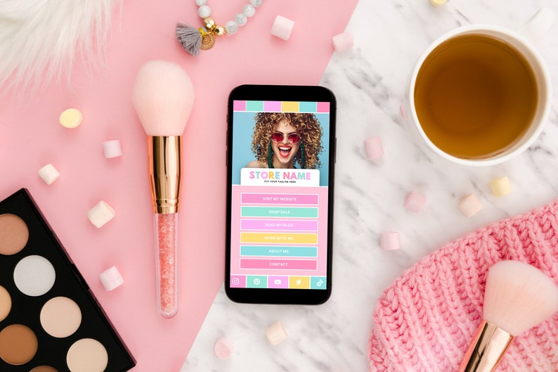 K&ouml;nnte beinhalten: Ein Smartphone, auf dem eine Website f&uuml;r ein Gesch&auml;ft namens "STORE NAME" angezeigt wird. Die Website enth&auml;lt Links zu "Besuchen Sie meine Website", "Shop Sale", "Shop Our Brand", "Was wir tun", "&Uuml;ber mich" und "Kontakt". Das Telefon befindet sich auf einer rosa und wei&szlig;en Oberfl&auml;che mit Make-up-Pinseln, einer Make-up-Palette und anderem Zubeh&ouml;r.