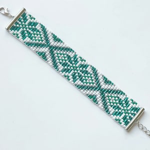 May include: A white and green beaded bracelet with a silver clasp. The bracelet features a geometric pattern.
