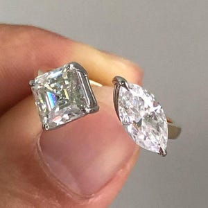May include: A silver ring featuring two large, clear gemstones. One is a square-cut diamond, and the other is a marquise-cut diamond. The ring's design allows the gemstones to sit side-by-side, creating a unique and elegant look.