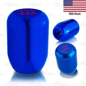 May include: Three blue car shift knobs with red lettering. The shift knobs are in different positions, showing the top and side views. The text on the top of the shift knobs reads "135" and "24R". The image also includes a small American flag.