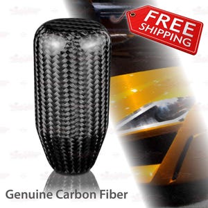 May include: A black carbon fiber shift knob with a woven pattern. The text "Genuine Carbon Fiber" is at the bottom of the image. The shift knob is a car accessory.