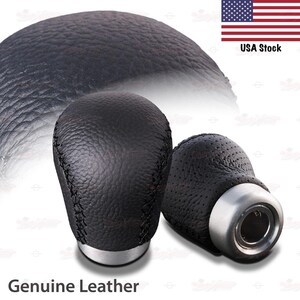 May include: Two black leather shift knobs with silver bases. One knob is solid, the other has a perforated design. The text "Genuine Leather" is at the bottom of the image.