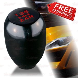 May include: A black gear shift knob with red gear markings. The shift pattern is 1, 3, 5, H, 2, 4, and R. The knob has a glossy finish and a rounded top. The background includes a yellow and black design.