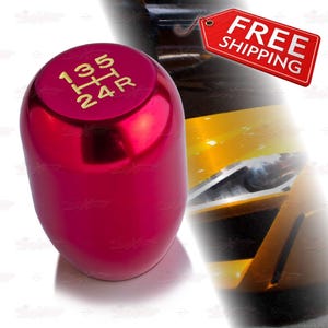 May include: A shiny, red shift knob with gold lettering indicating gear positions. The knob has a smooth, rounded shape and is designed for a vehicle's manual transmission. The image also includes a red tag with the words "FREE SHIPPING".