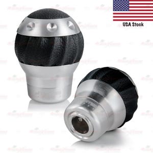 May include: Two black and silver car shift knobs. The top portion is black with a textured leather-like appearance, and the bottom is silver. The knobs have a modern design and are likely for a vehicle's gear shift.