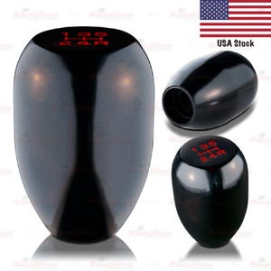 May include: Glossy black shift knob with red gear markings. The knob has a smooth, rounded shape and features the gear pattern 1, 2, 3, 4, 5, and R. The image shows the knob from multiple angles.