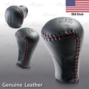 May include: Black leather shift knob with red stitching. The knob features gear markings and the text "Genuine Leather". The image also includes a USA flag and the text "USA Stock".