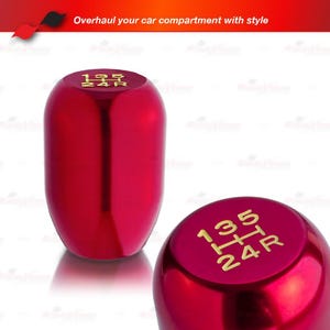 May include: A pair of shiny red car shift knobs. The top of each knob has gold lettering indicating the gear positions. The text "Overhaul your car compartment with style" is at the top of the image.