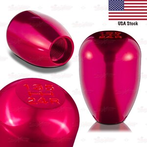 May include: A set of three shiny, magenta-colored car shift knobs. One knob is shown from the side, revealing internal threading. Another shows the top with the gear pattern 135/24R. The third knob is shown from the front. The text "USA Stock" is visible.