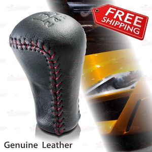 May include: Black leather gear shift knob with red stitching. The knob has a stitched pattern and the text "Genuine Leather" is at the bottom. The image also includes a red tag with the text "FREE SHIPPING".