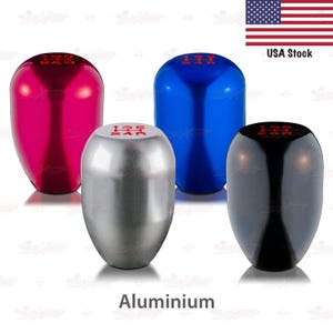 May include: Four aluminum shift knobs in pink, silver, blue, and black. Each knob has red lettering indicating gear positions. The word "Aluminium" is printed at the bottom of the image.