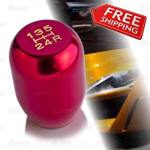 May include: A shiny, red shift knob with gold lettering indicating gear positions. The knob has a smooth, rounded shape and is designed for a vehicle's manual transmission. The image also includes a red tag with the words "FREE SHIPPING".