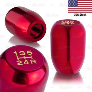 May include: Red car shift knobs with gold lettering indicating gear positions. The knobs have a glossy finish and a threaded interior for easy installation. The image includes a USA stock flag.