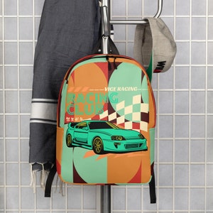 May include: A green and orange backpack with a chequered flag design and a cartoon car. The backpack has the text "Vice Racing" and "Racing Club" on it. The car is a green sports car with the text "在深夜" on it.