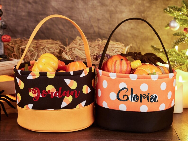 May include: Two Halloween trick-or-treat bags with orange and black fabric. One bag has a candy corn pattern and the name "Jordan" embroidered on it. The other bag has white polka dots and the name "Gloria" embroidered on it.