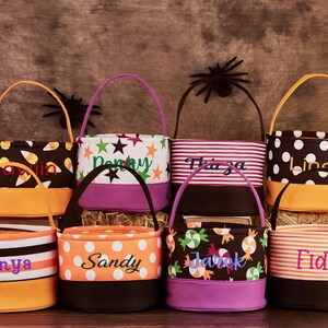 May include: Eight Halloween trick-or-treat bags with personalized names. The bags are made of fabric and have different patterns, including candy corn, stars, stripes, and polka dots. The bags are in various colors, including orange, black, purple, and brown.