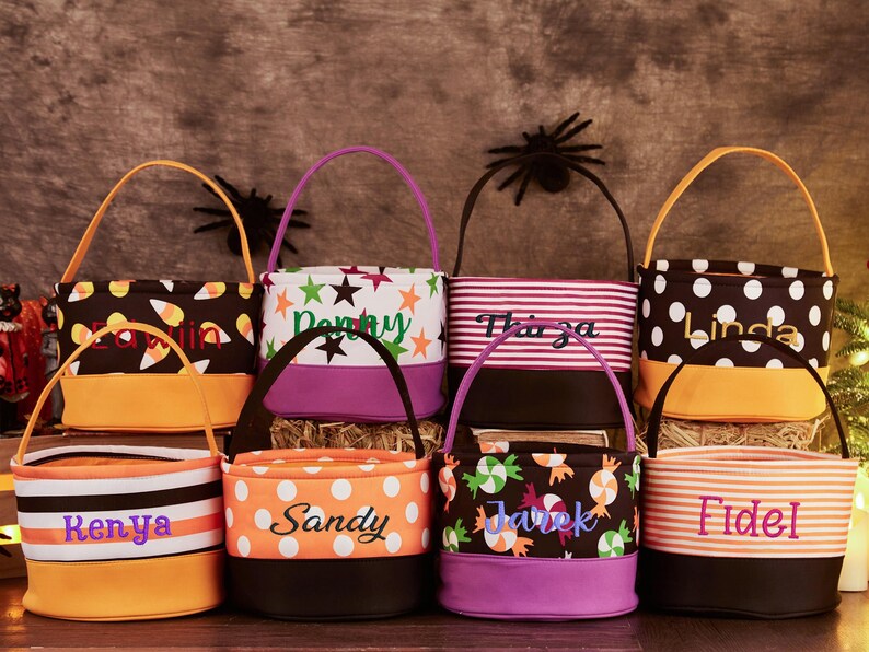 May include: Eight Halloween trick-or-treat bags with personalized names. The bags are made of fabric and have different patterns, including candy corn, stars, stripes, and polka dots. The bags are in various colors, including orange, black, purple, and brown.