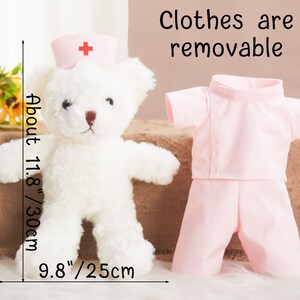 May include: A white teddy bear wearing a pink nurse's uniform with a red cross on the hat. The teddy bear is 11.8 inches tall and 9.8 inches wide. The clothes are removable.