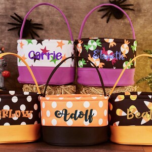 May include: Five Halloween trick-or-treat bags with different patterns and personalized names: Barlow, Adolf, Beata, Carrie, and Elspeth. The bags are made of fabric and have a purple, orange, or black trim.
