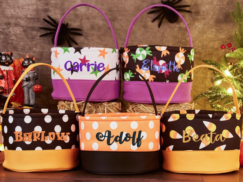 May include: Five Halloween trick-or-treat bags with different patterns and personalized names: Barlow, Adolf, Beata, Carrie, and Elspeth. The bags are made of fabric and have a purple, orange, or black trim.