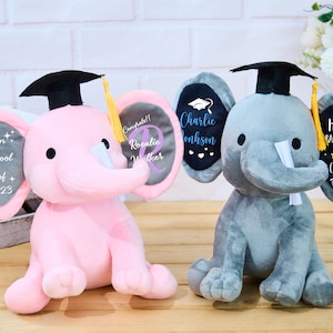 Puede incluir: Dos peluches de elefante de graduaci&oacute;n, uno gris y otro rosa, que llevan gorros de graduaci&oacute;n negros con borlas amarillas. El elefante gris tiene una oreja negra con el texto "Charlie Johnson" y la otra oreja tiene el texto "Happy Graduation!! Class of 2023". El elefante rosa tiene una oreja gris con el texto "Madison High School Class of + 2023" y la otra oreja tiene el texto "Congrats!! Rosalie Walker".
