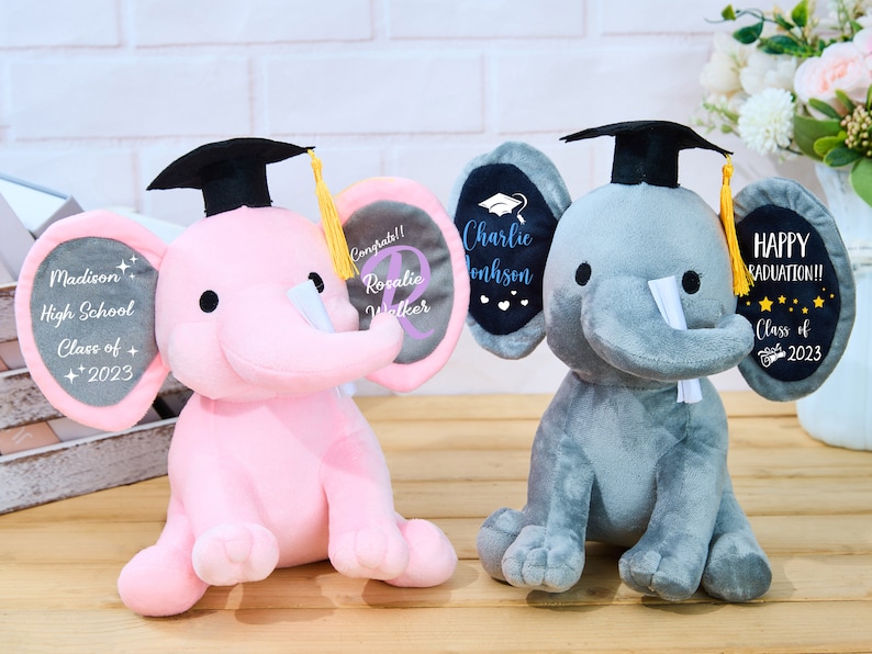 Puede incluir: Dos peluches de elefante de graduaci&oacute;n, uno gris y otro rosa, que llevan gorros de graduaci&oacute;n negros con borlas amarillas. El elefante gris tiene una oreja negra con el texto "Charlie Johnson" y la otra oreja tiene el texto "Happy Graduation!! Class of 2023". El elefante rosa tiene una oreja gris con el texto "Madison High School Class of + 2023" y la otra oreja tiene el texto "Congrats!! Rosalie Walker".