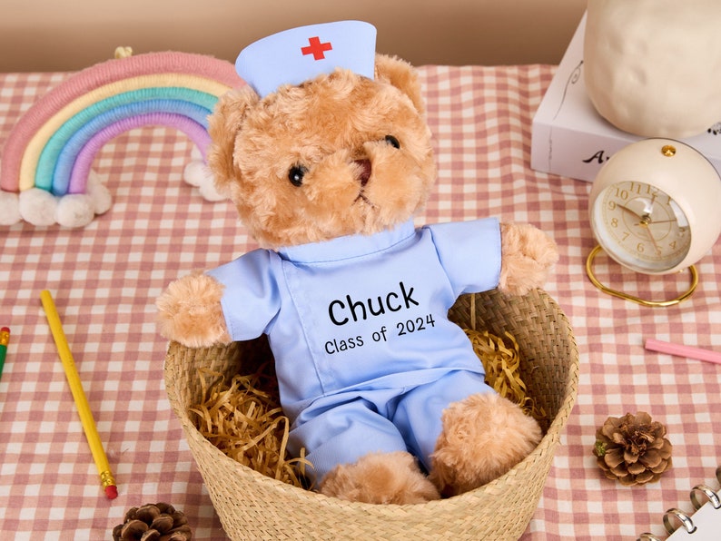 May include: A light blue teddy bear wearing a nurse's hat and scrubs. The bear has a name tag that says "Chuck Class of 2024".