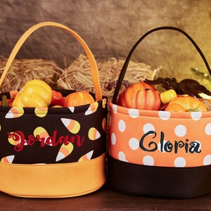 May include: Two Halloween trick-or-treat bags with orange and black fabric. One bag has a candy corn pattern and the name "Jordan" embroidered on it. The other bag has white polka dots and the name "Gloria" embroidered on it.