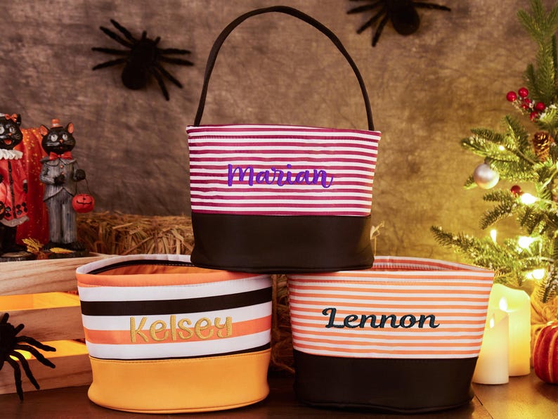 May include: Three striped Halloween trick-or-treat bags with black handles. The bags are personalized with the names "Marian", "Kelsey", and "Lennon".