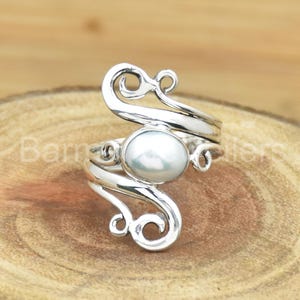 May include: A silver ring with a white pearl set in a swirling design.