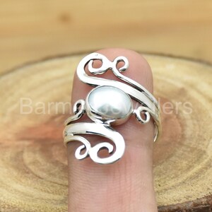 May include: A silver ring with a white pearl set in a swirling design.