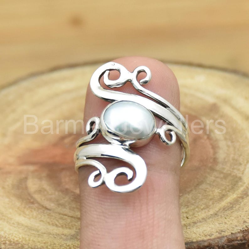 May include: A silver ring with a white pearl set in a swirling design.