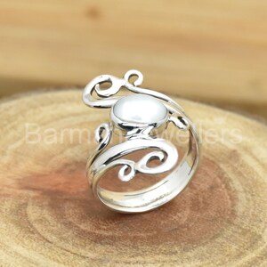 May include: A silver ring with a white pearl set in a swirling, ornate design.