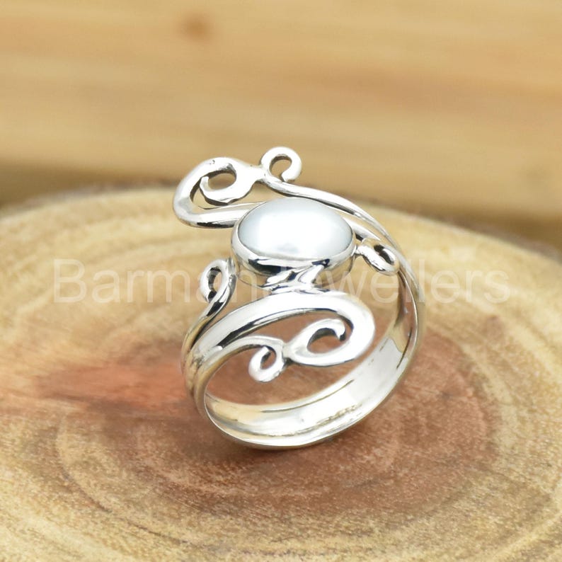 May include: A silver ring with a white pearl set in a swirling, ornate design.