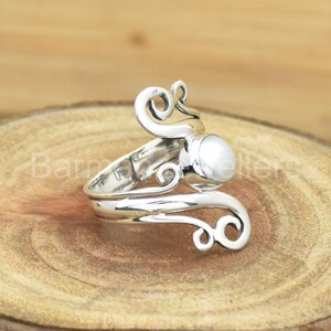 May include: A silver ring with a white pearl set in a swirling design.