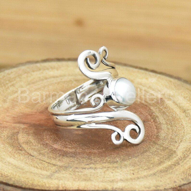 May include: A silver ring with a white pearl set in a swirling design.