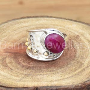 May include: A silver ring with a hammered texture and a large, oval-shaped, pink gemstone set in the center. The ring has gold accents around the gemstone and on the band.
