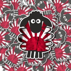May include: A black sheep silhouette with a red and white rising sun design, reminiscent of the Japanese flag. The sheep is surrounded by other sheep silhouettes with the same design.