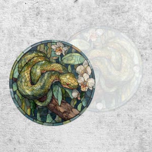 May include: Circular coaster with a design of a green snake on a branch, surrounded by white flowers and green leaves. The coaster has a stained glass effect and a dark blue border.