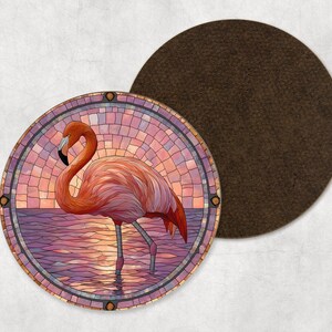 May include: A circular coaster with a stained-glass effect flamingo design in pink, orange, and purple hues. The flamingo is depicted in water against a sunset backdrop. A separate, plain brown coaster is also present.