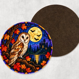 May include: A circular coaster featuring a stained glass style illustration of a barn owl perched on a tree branch with orange autumn leaves. The background shows a full yellow moon, flying bats, a dark castle, mountains, and a lake.