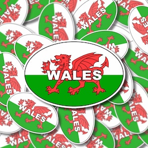 May include: A close-up of a red dragon with a white outline on a green and white oval sticker. The sticker says "WALES" in white letters. The sticker is surrounded by other similar stickers with the same design.