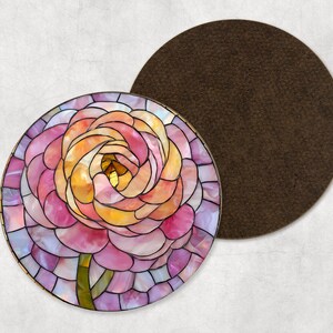 May include: A circular coaster featuring a stained glass design of a flower in shades of pink, yellow, and orange. A separate brown coaster sits beside it. The flower has a green stem.