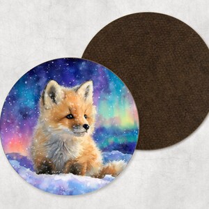 May include: A circular coaster with a watercolour painting of a fox cub in a snowy scene under the aurora borealis. The coaster has a brown backing. The fox has orange fur and is sitting in the snow.