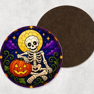 May include: A round coaster featuring a stained glass style illustration of a white skeleton sitting next to an orange jack-o'-lantern. The background shows a yellow moon, purple clouds, and yellow stars. The coaster has a dark brown felt backing.