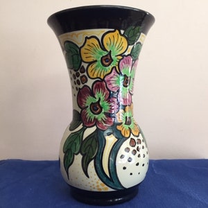 Może przedstawiać: Ceramiczny wazon z ciemnoniebieską podstawą i białym korpusem. Wazon jest ozdobiony kwiatowym wzorem w odcieniach żółtego, różowego, zielonego i brązowego.