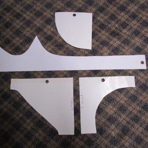 May include: A collection of white paper templates with various shapes, including curved and angular designs. Each template has a small hole, likely for hanging or marking. The templates are arranged on a patterned brown and gray surface.