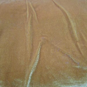 Puede incluir: Primer plano de una tela de terciopelo marr&oacute;n dorado con sutiles reflejos y pliegues. El material suave tiene un brillo lujoso, con luz que se refleja en la superficie texturizada. El color de la tela es un tono c&aacute;lido y acogedor.